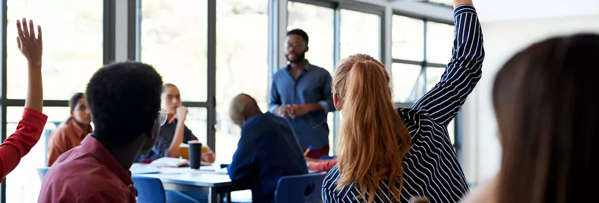 a university classroom with several students with their hands up