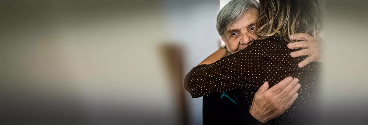 an elderly woman being hugged by a younger woman