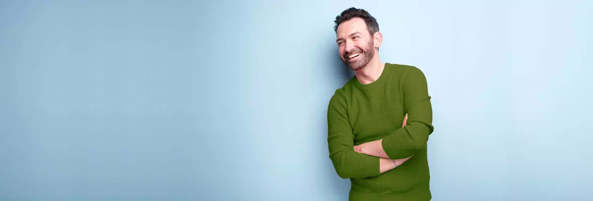 young man in green jumper with a smile on his face leaning against a blue background