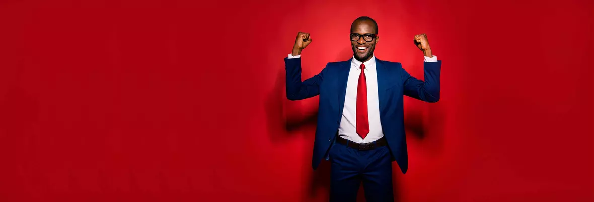 a young smartly dressed man in a red tie celebrating in front of a red background