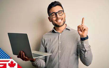 man, smiling and holding laptop; other hand raised, pointing upwards