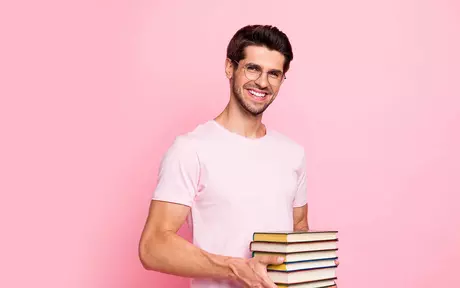young man in glasses holding several books