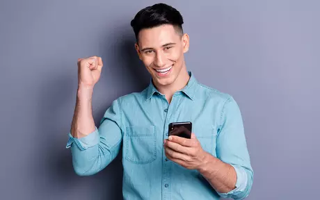 man with blue shirt holding phone celebrating