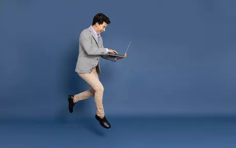 Man in suit holding laptop jumping