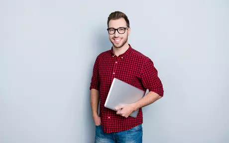 Smilende mann i rød og svart skjorte med PC under armen og grå bakgrunn