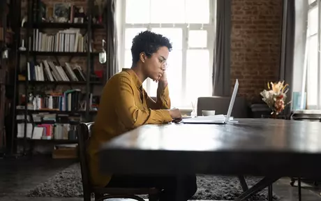 Woman sitting at at table thinking, looking at a computer