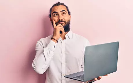 Bearded man thinking and holding a computer