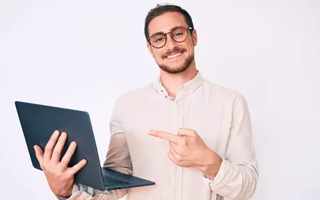 Smiling man with glasses pointing at computer 