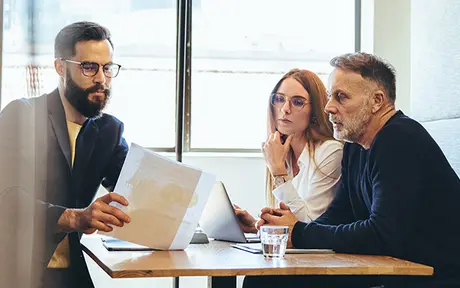 Three individuals seated around a wooden table in a professional setting, engaged in a collaborative discussion.