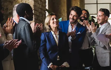 A group of people applauding a woman in a suit, celebrating a success in a bright room. 