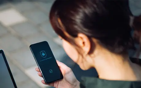 A person is holding a smartphone displaying a lock icon and a security-related interface, suggesting device protection or authentication.