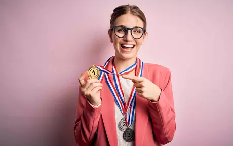 a young woman smiling and pointing to a 1st place Gold medal around her neck