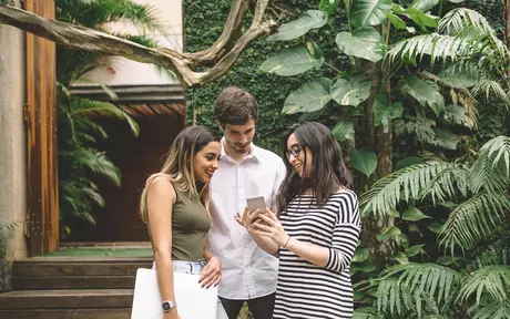 a young man and two young women looking at a mobile phone screen