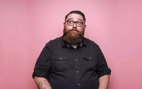 a happy bearded hipster in glasses in front of a pink background 