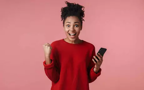 a young woman in a red jumper holding a mobile phone and looking excited