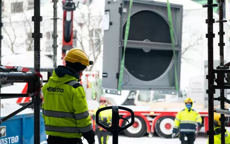 Man with a hardhat and a yellow coat with Elektrogruppen logo on the back on a buliding site