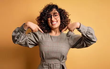 Smiling woman with glasses pointing down with both hands