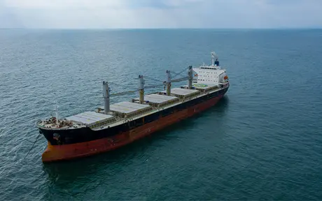 A large cargo ship sails on a vast, calm sea under a cloudy sky.