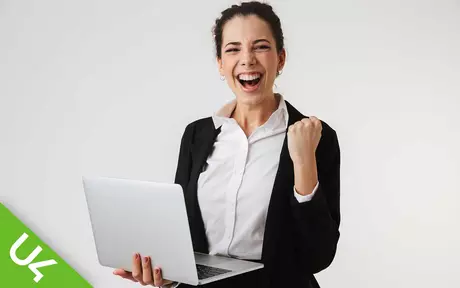 Woman holding laptop in one hand, other hand clenched in celebration
