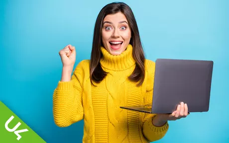 Woman holding laptop in one hand, other hand clenched in celebration